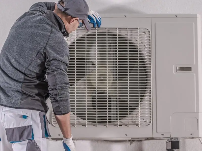 Man looking at a heat pump up a ladder