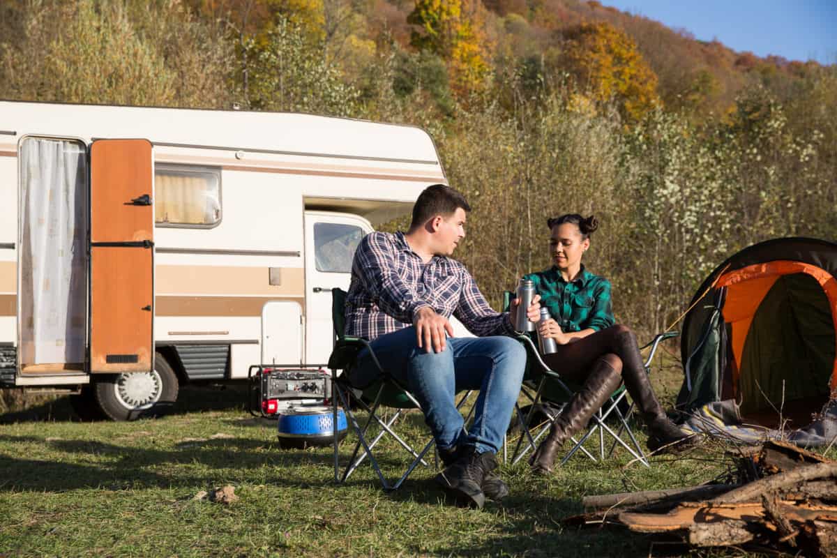 Couple Enjoying Their Holiday In A Mountain Camps Site. Couple Camping With Retro Camper Van With A Generator.