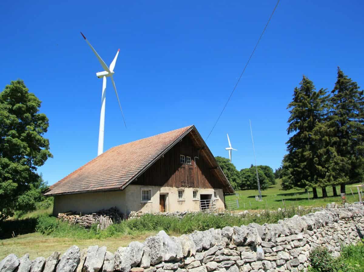 Small House Made Of Wood And White Wind Turbines In The Country By Beautiful Weather.