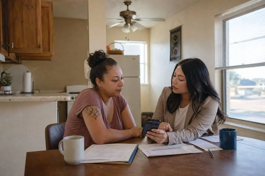 A utility assistance advocate meets with a family violence survivor at a kitchen table in a Texas apartment.