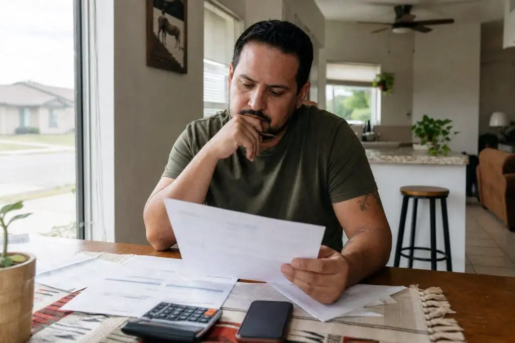 A Texas renter compares electricity service documents at a kitchen table with a phone and calculator.